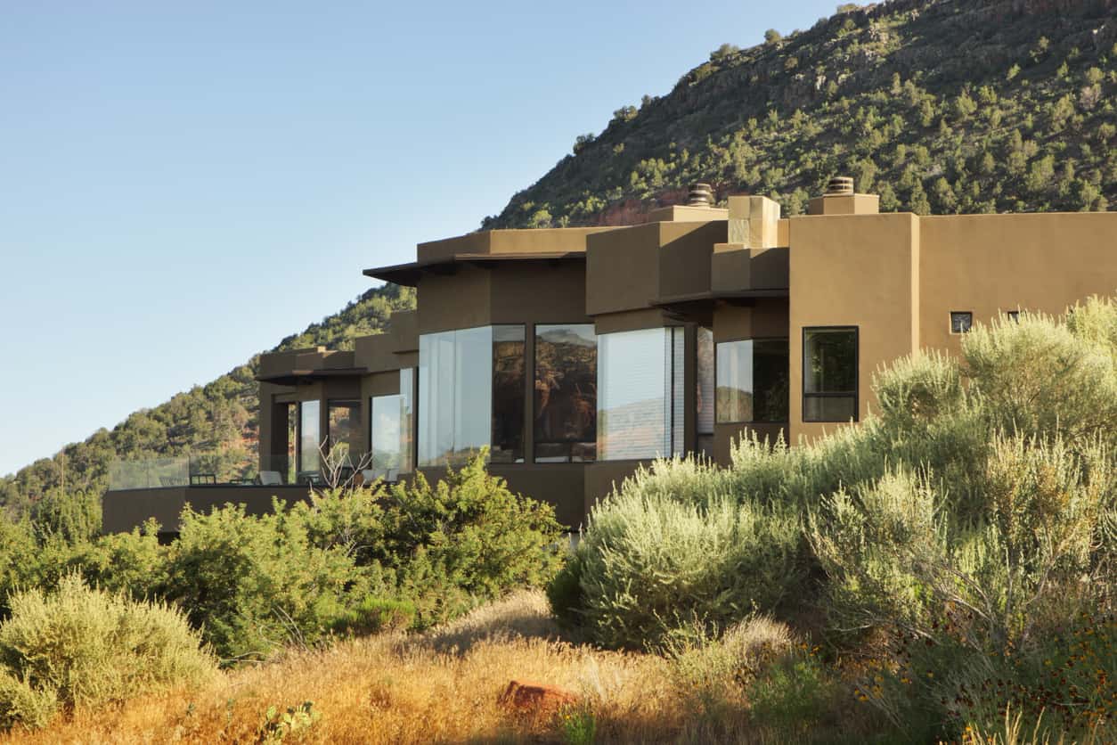 粉刷的豪华房子，有玻璃窗户，在山脚下，周围都是沙漠植物。