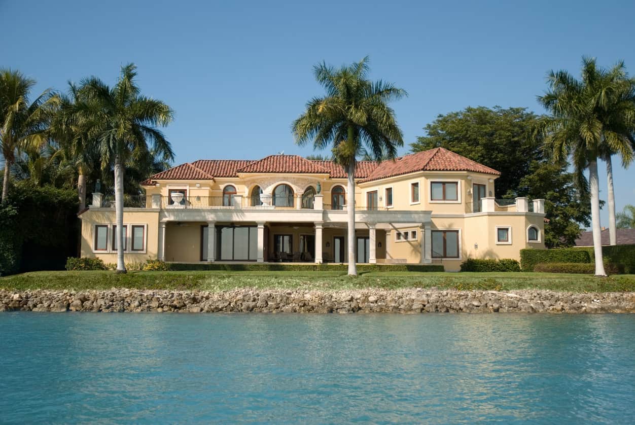 一个大的海滨房子，有盒子状的树篱和棕榈树。