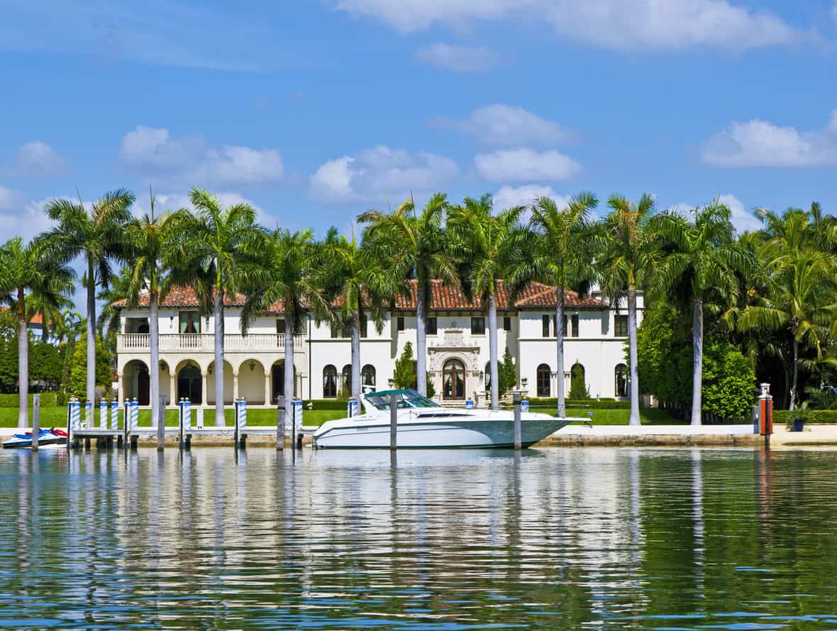 一排棕榈树矗立在豪华的海滨别墅和停靠在港口的游艇前。