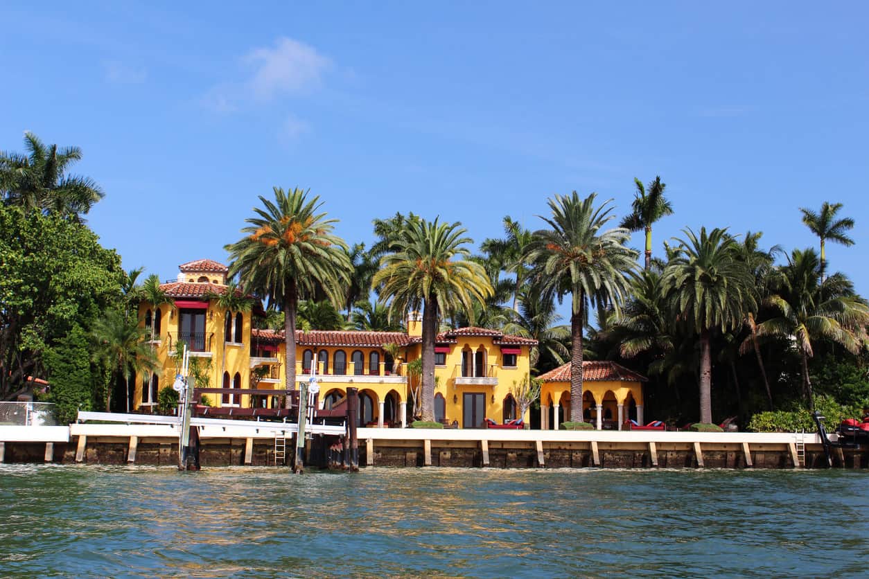 明亮的黄色豪华海滨别墅，四周环绕着棕榈树，天空湛蓝。