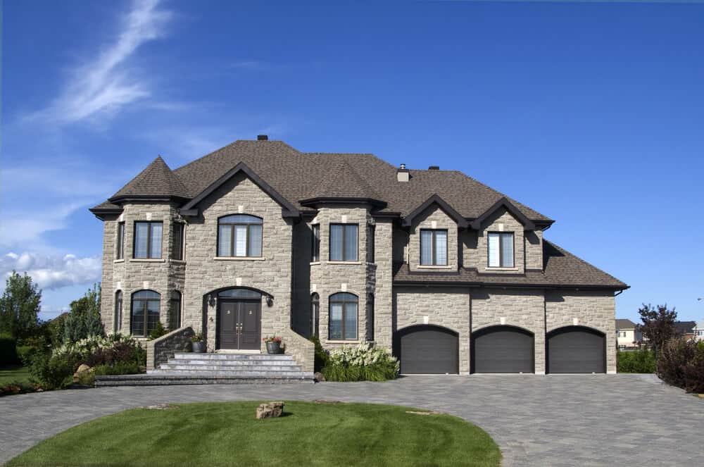 一座巨大的石头房子，带有淡淡的浅棕色调。它有3个车库和一个宽敞的区域在前面，这是一个完美的景观创意。