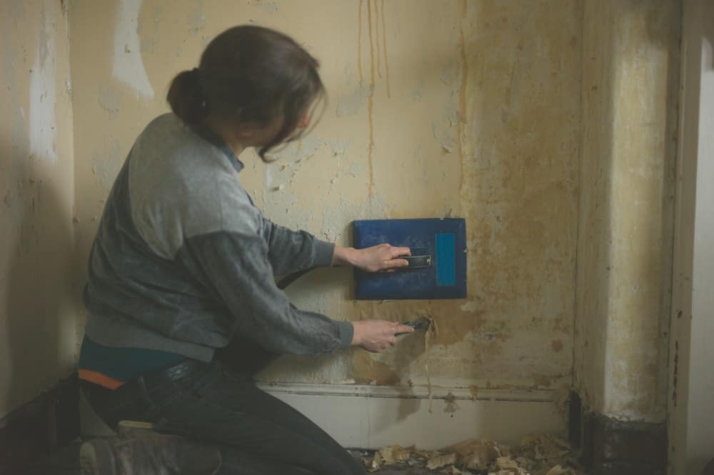 一位女士正在用蒸笼去除旧墙纸。