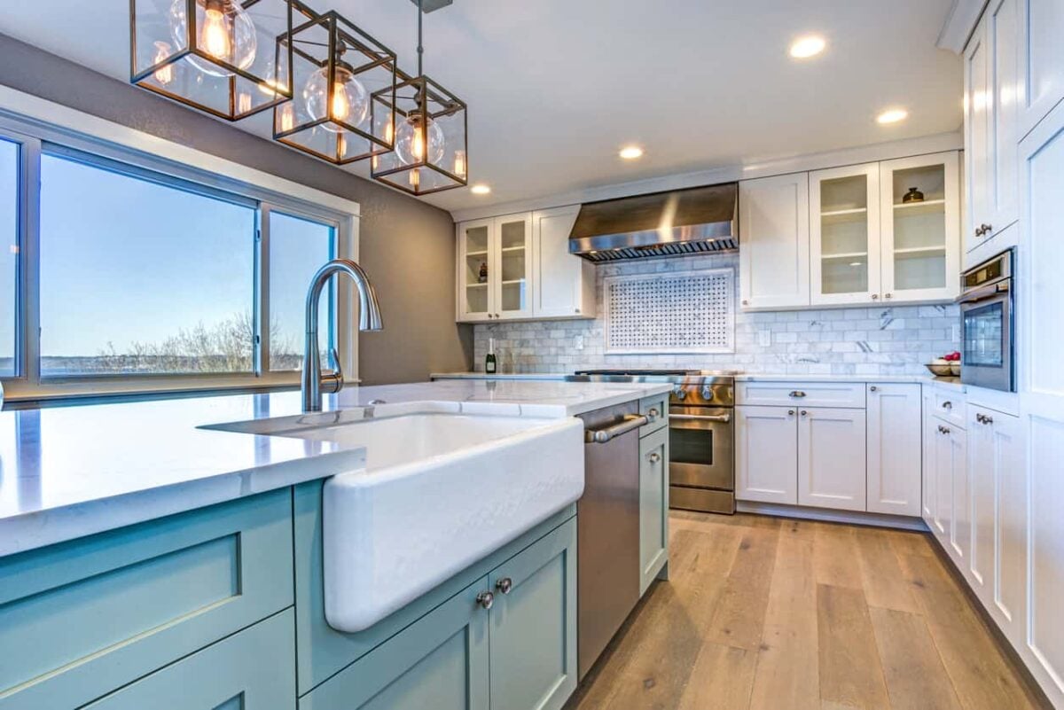 厨房配有蓝色岛台、大型白色农家乐水槽、白色橱柜和宽板硬木地板，所有厨房都配有现代单体吊灯和嵌入式灯。