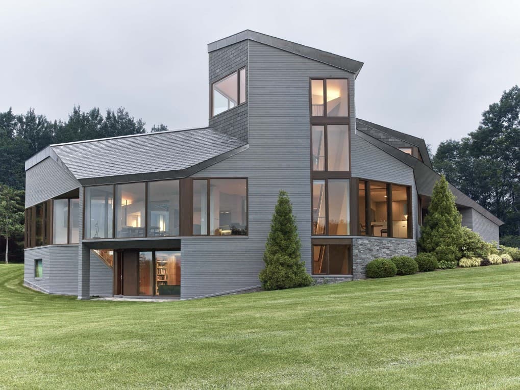 这座山中的房子有着时尚的外观，以灰色的外观为特色，周围环绕着一个广阔而美丽的草坪区域。