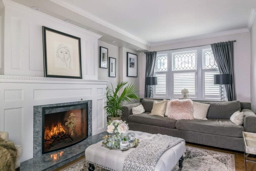 传统的正式客厅，白色表面壁炉(有漂亮的造型)，周围是灰色的传统客厅家具，包括一个优雅的白色簇绒方凳，用作咖啡桌。