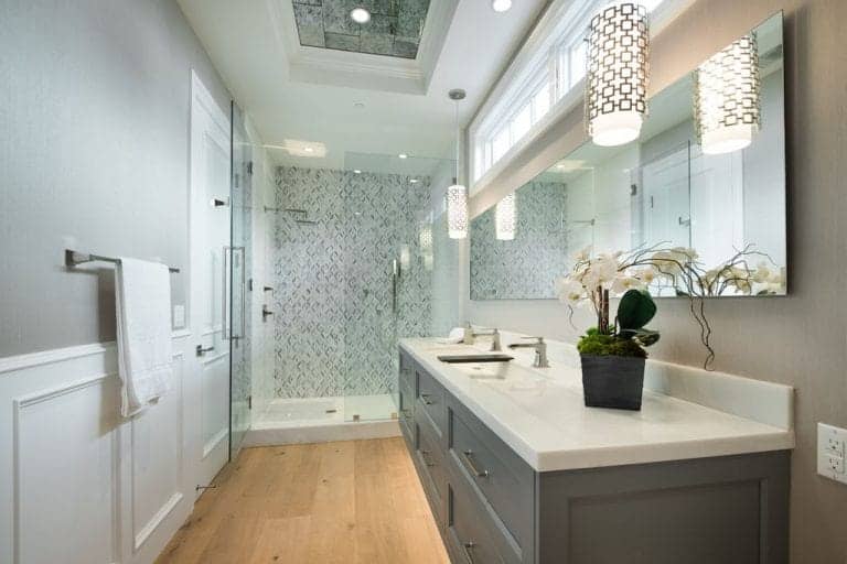 灰色浴室，带有浮动洗手池和安装在白色护壁板上的不锈钢毛巾架。它包括一个步入式淋浴间，以钻石图案瓷砖为特色。