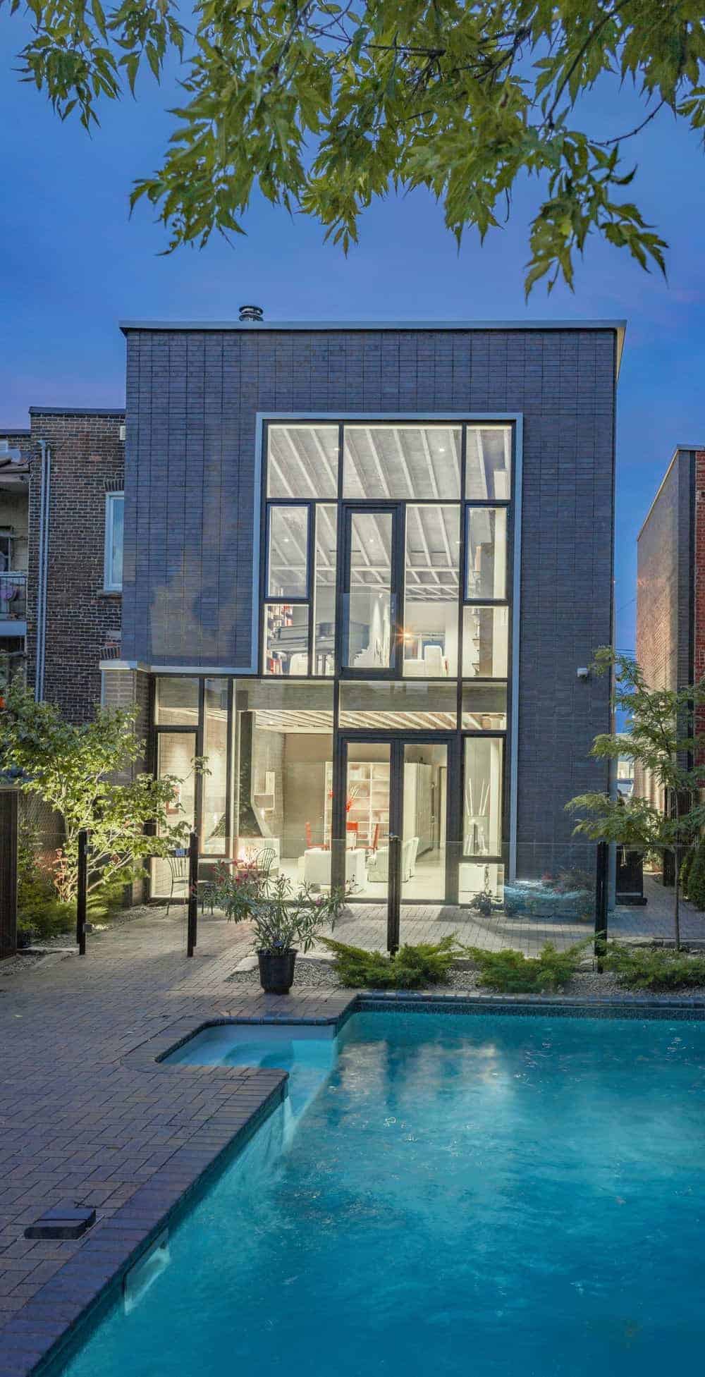 这座灰色外观的现代住宅以砖砌的走道为特色，周围种着健康的植物和树木。这所房子还有一个游泳池。