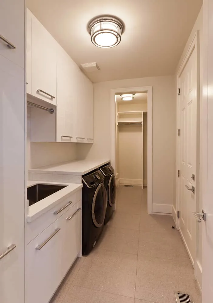 所有白色窄,长洗衣房大量的存储空间和长矩形水槽旁边的洗衣机。