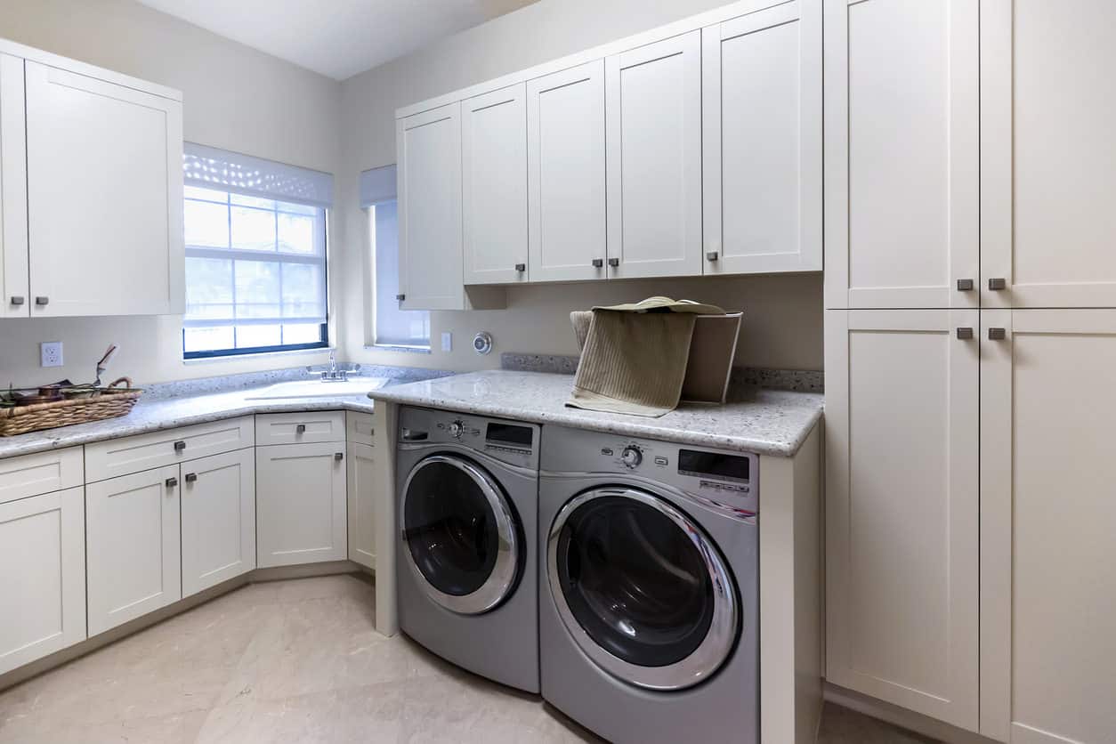传统风格的大型洗衣房，定制的白色橱柜，角落水槽和不锈钢洗衣机和烘干机。