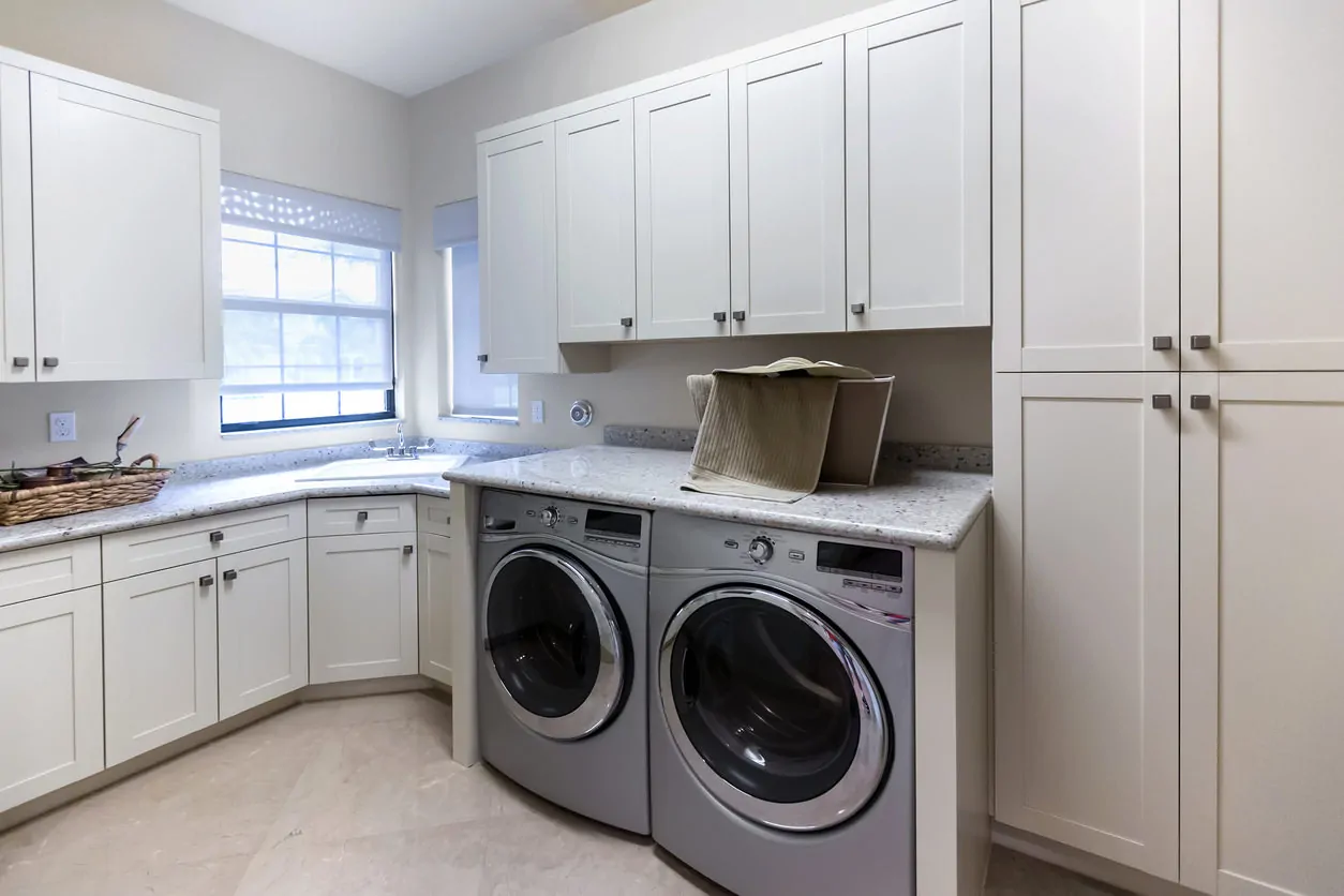 传统风格自定义构建的大型洗衣房白色橱柜、角落水槽和不锈钢洗衣机和干衣机。