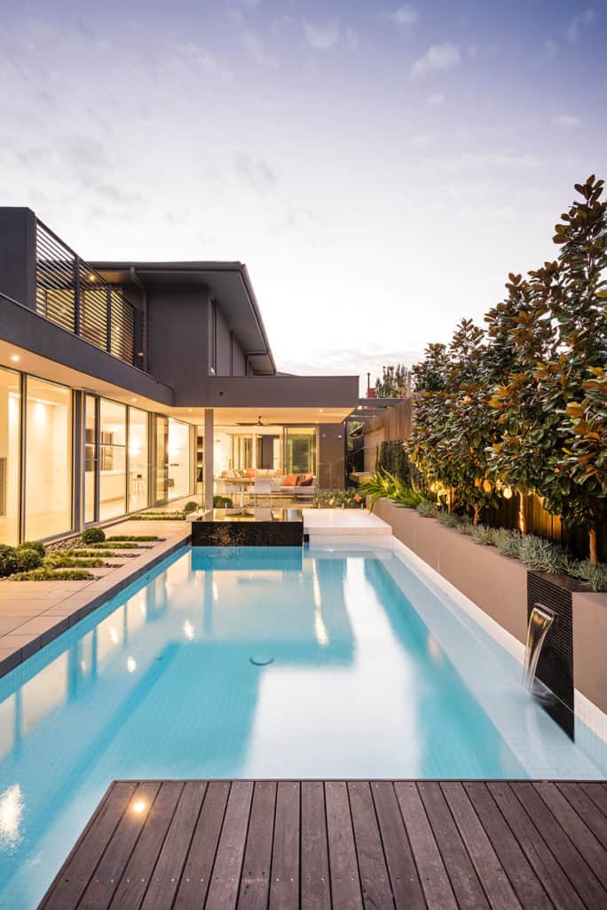 一个现代的灰色房子，有一个休闲的户外区域，游泳池被植物和树木包围。