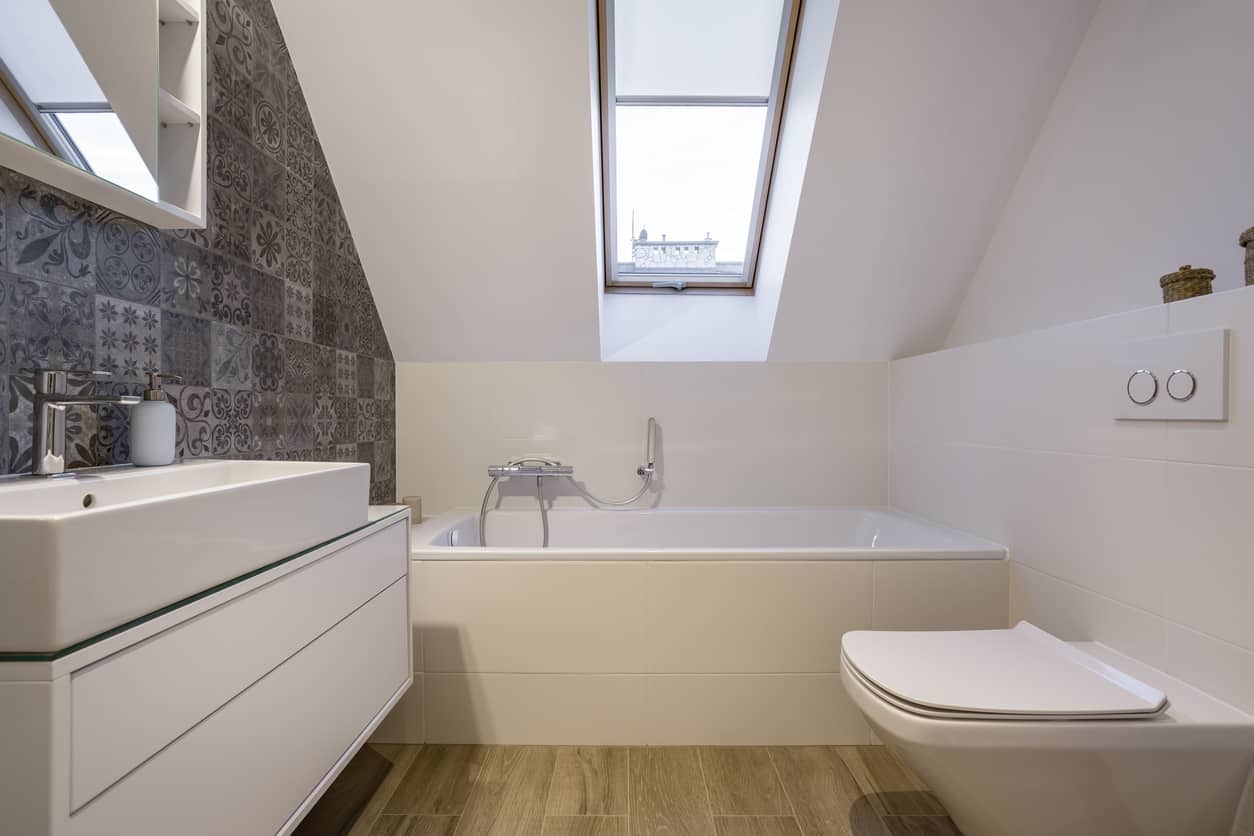 阁楼上的小主浴室带天窗，小浴缸和长槽状的现代水槽。
