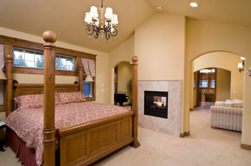 地中海风格的主卧室，地毯地板和米黄色墙壁。房间提供一张优雅的床和一个壁炉，由一个令人惊叹的吊灯照明。