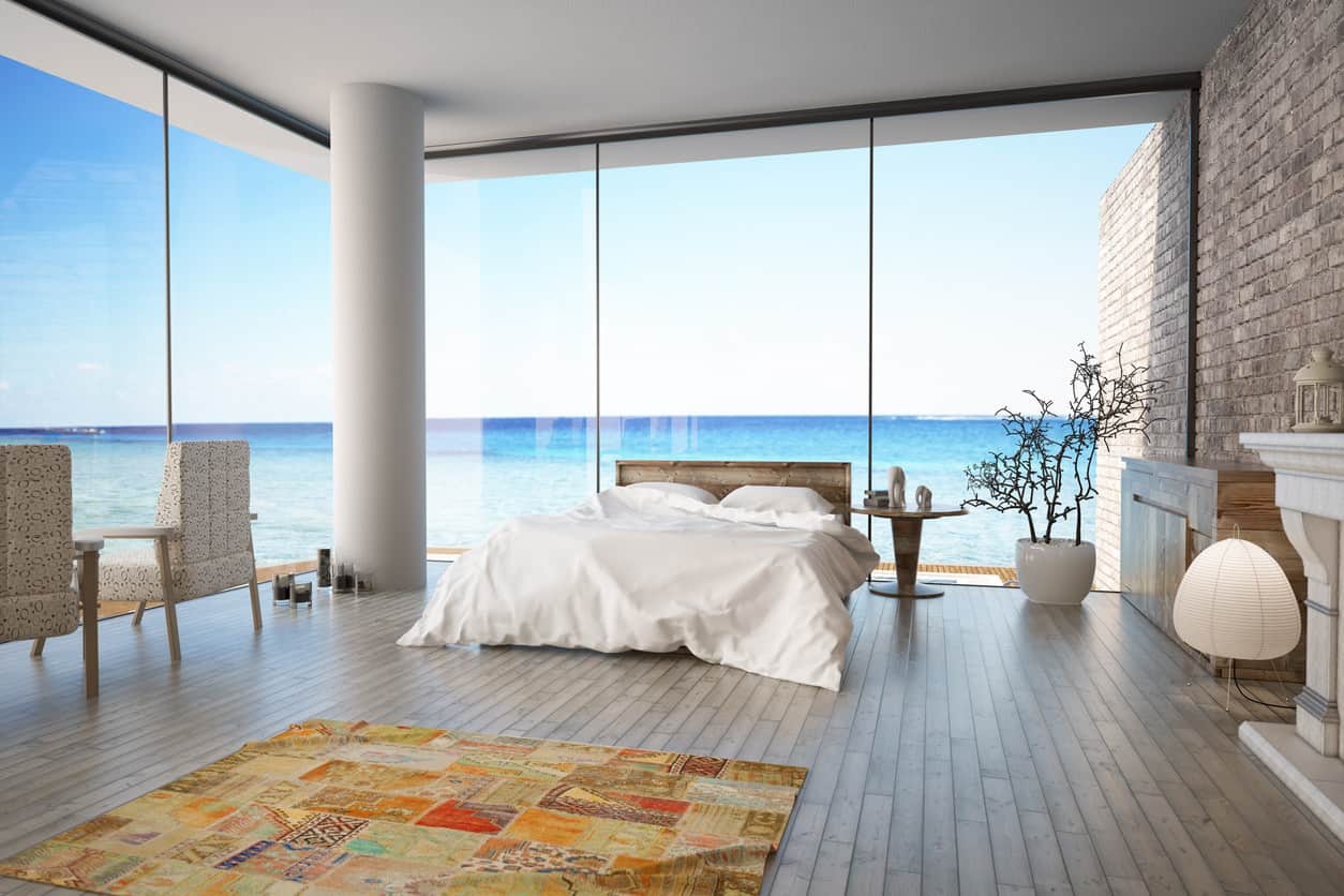 海景现代主卧室，砖墙，木地板，彩色地毯，纯白色天花板和令人难以置信的落地窗。