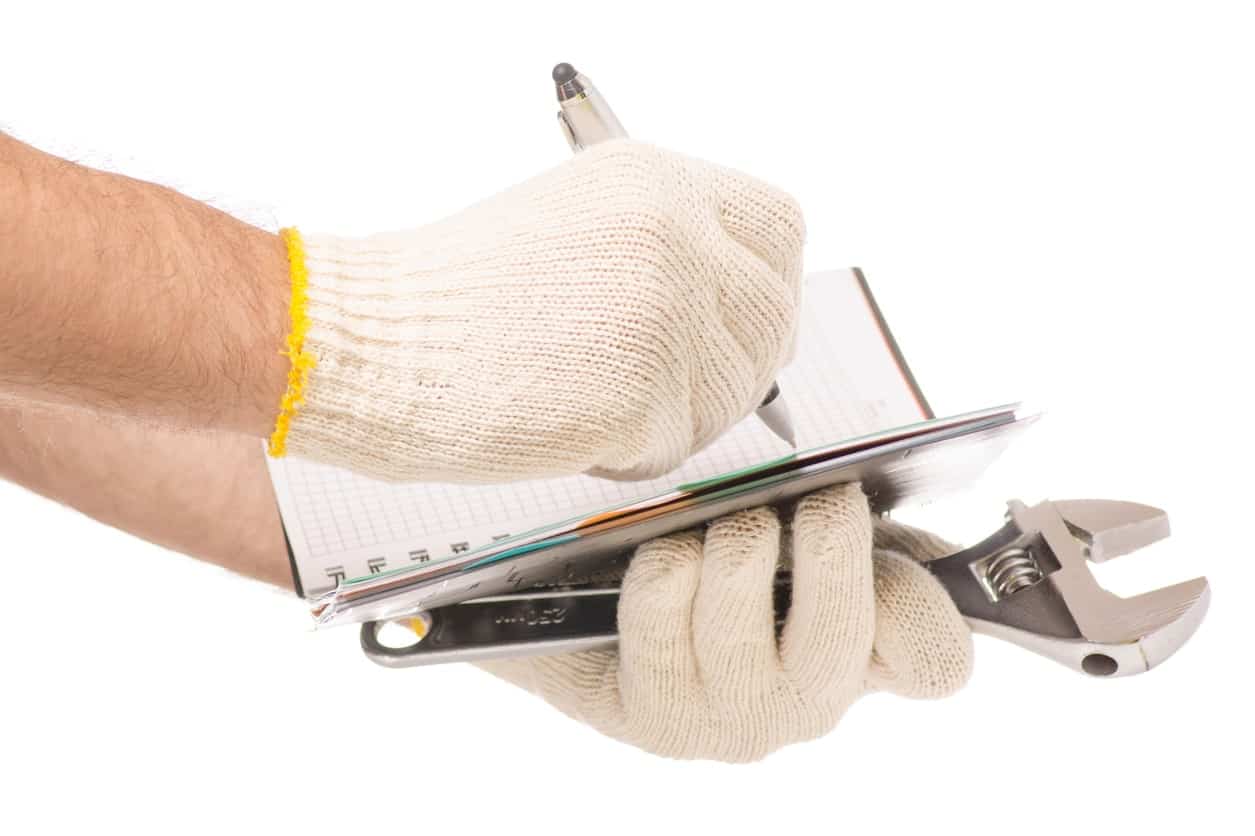 戴着保护手套的双手在笔记本上写字，手里拿着工具。