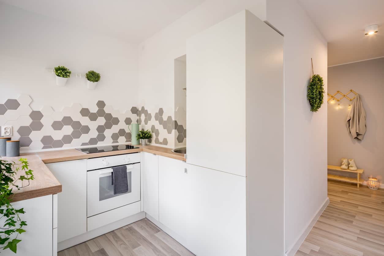 白色极简主义小厨房，木质台面。白色和灰色的六边形瓷砖后挡板为空间增添了有趣的纹理。