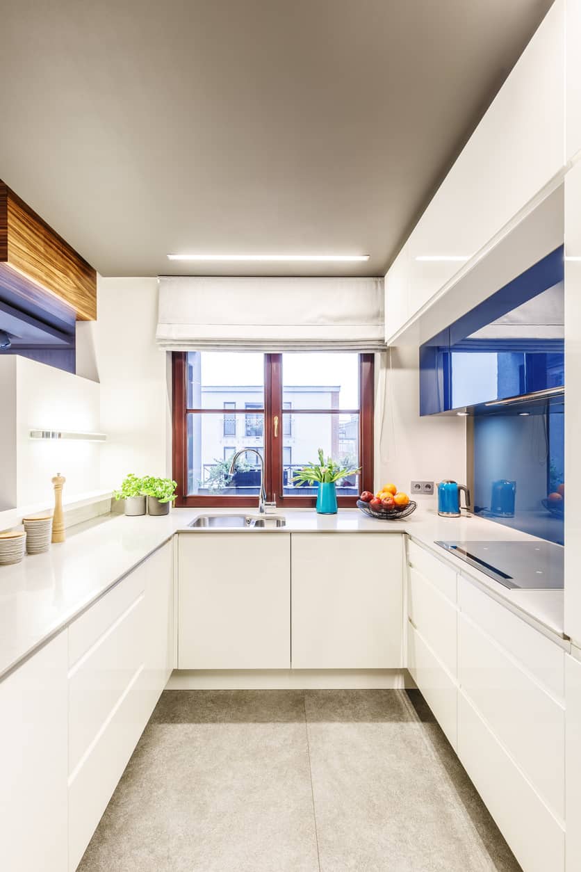 现代蓝白相间的u形小厨房，水槽上方有窗户。