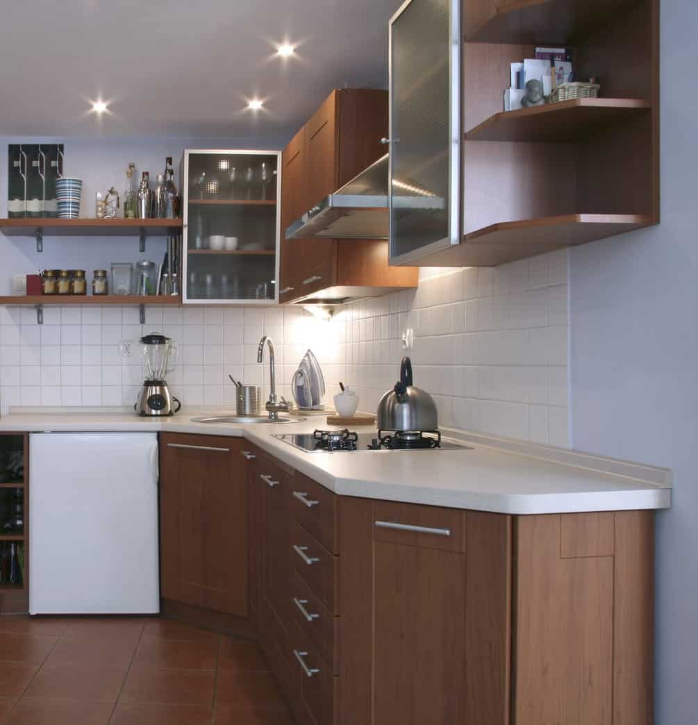 小l型厨房，现代木橱柜，开放式上置物架和白色后挡板。包括半冰箱和迷你炉灶。