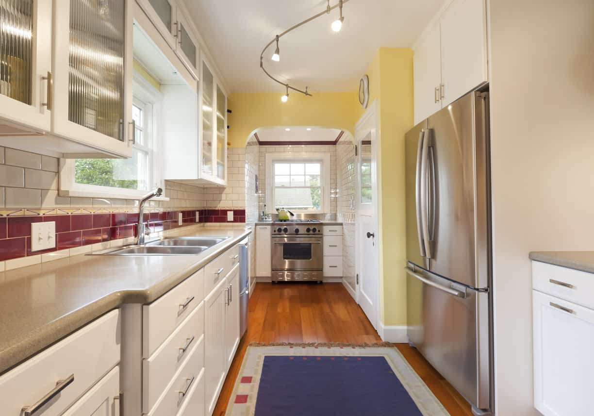狭长的la形厨房新装修，白色橱柜，黄色强调墙，不锈钢电器和木地板。再说一次，我不喜欢米色的台面，但我喜欢宝石红色的后挡板。
