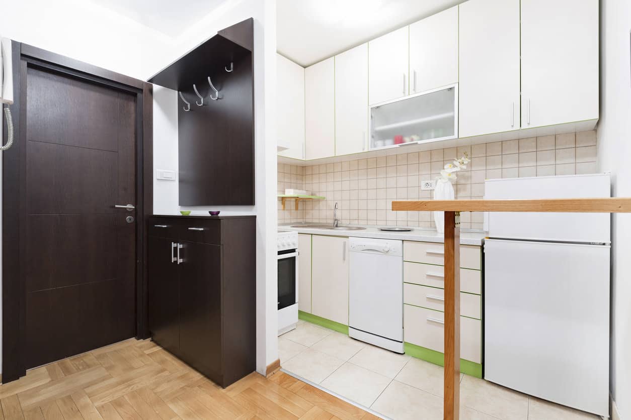 公寓里有一个l形的白色小厨房和绿色的踢脚板。小木制半岛早餐吧台将厨房空间与公寓入口隔开。