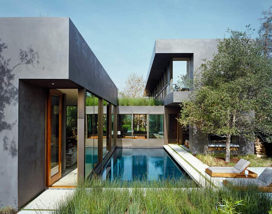 这是一座灰色外观的房子，带有一个游泳池，旁边有两个休息室。