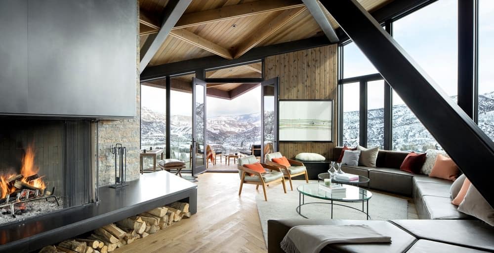 正式的客厅，高天花板，惊人的视野和巨大的定制组合沙发，面对现代滑雪小屋中的大型现代木壁炉