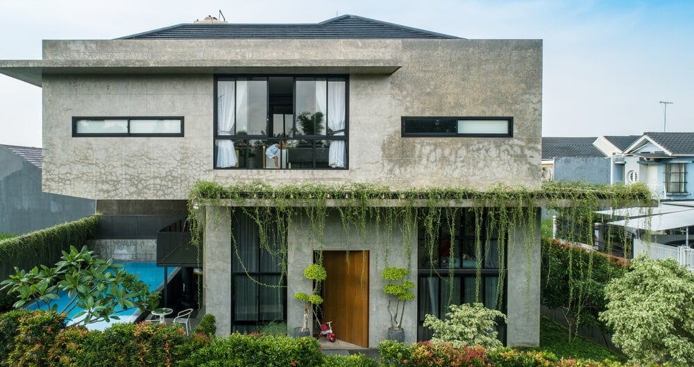 这是房子的正面，有各种窗户和玻璃墙装饰的混凝土外墙，以及悬挂的藤蔓和灌木景观。
