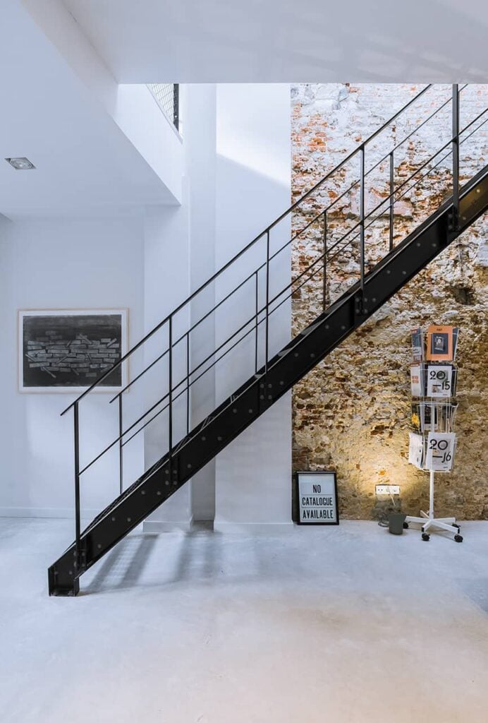 工业风格的楼梯框架与钢栏杆和黑色金属串在白色和石头的墙壁。它下面的空间是一个黑色的框架和金属丝旋转展示架。