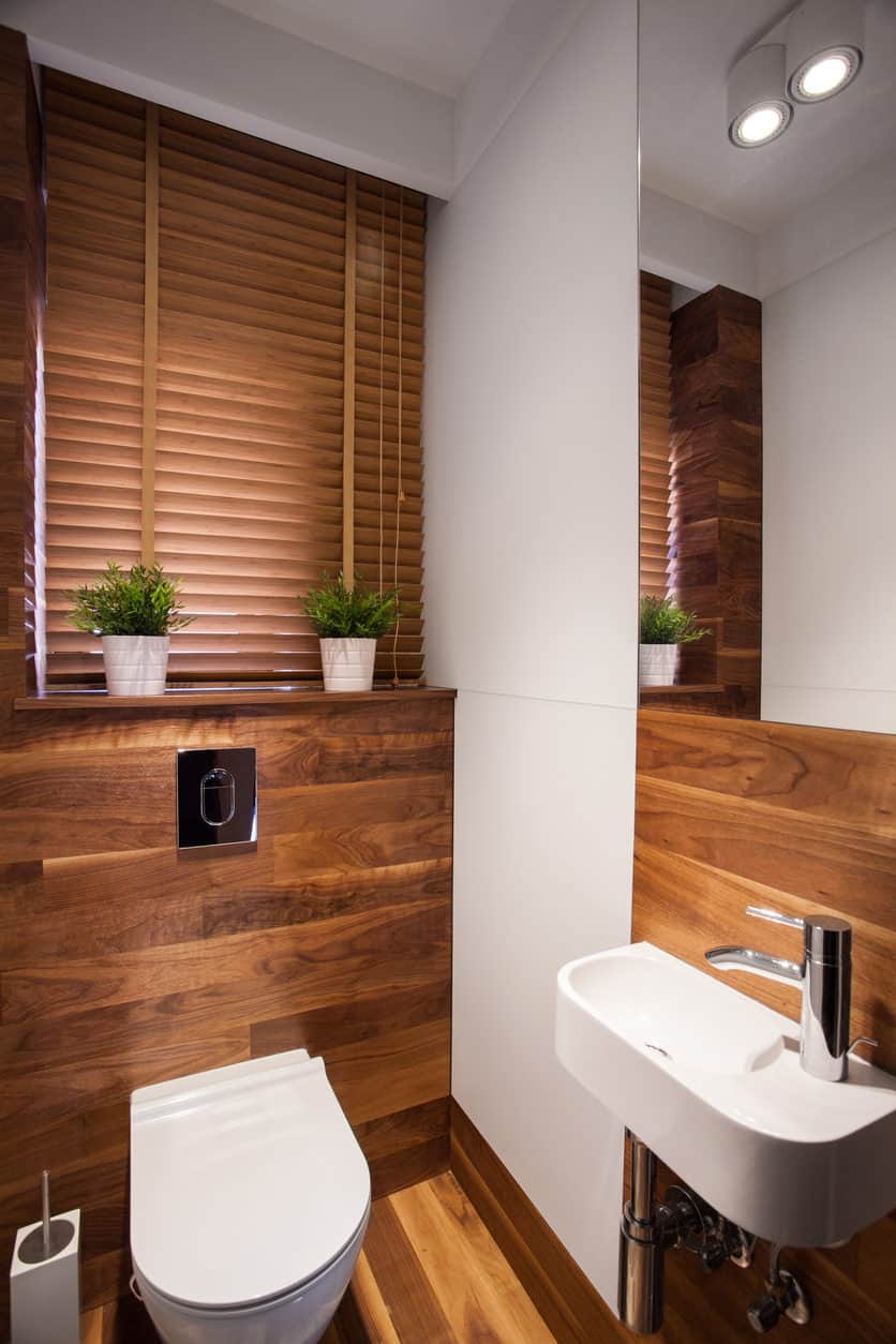木制的化妆间，棕色的百叶窗，带有自动冲洗系统的厕所，白色的水槽和天花板灯。