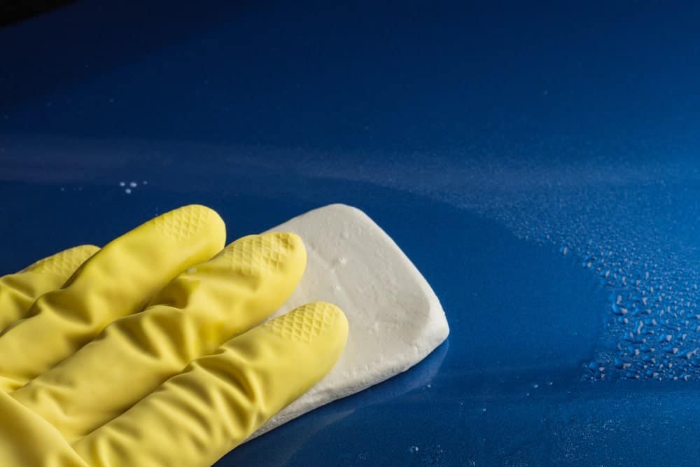 戴着手套的手放在汽车表面的泥条上。