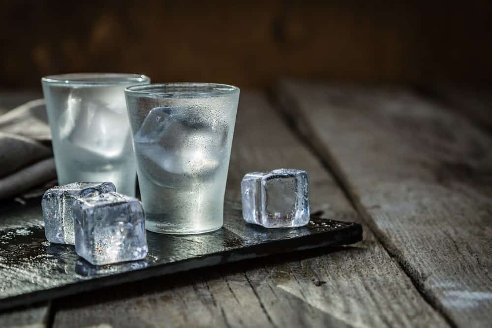 伏特加装在两个小酒杯里，冰块放在乡村的背景上。