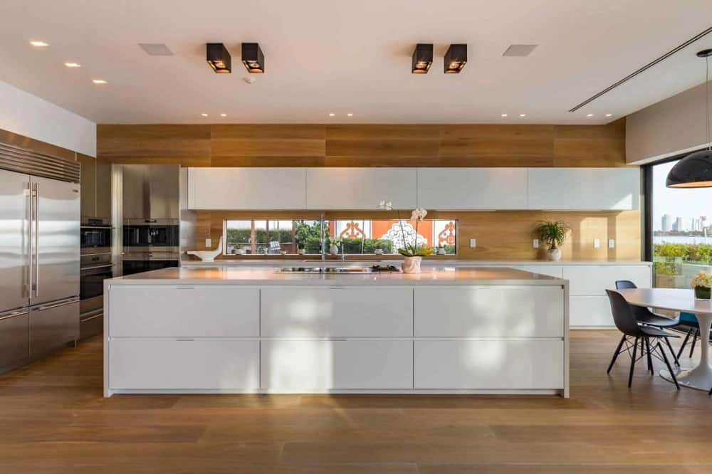 这是厨房的一个视角，它有一致的白色现代橱柜和白色厨房岛，与不锈钢电器和元素相匹配。硬木地板和墙板强调了这些。