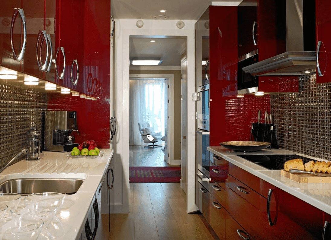 小厨房里的高光泽深红色橱柜，配有漂亮的镀铬后挡板，镀铬橱柜五金和不锈钢电器，与白色台面进一步抵消。