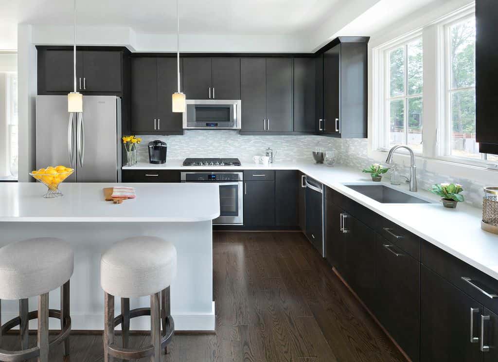 黑色过渡厨房设计，当代黑色橱柜，不锈钢五金，不锈钢电器和深色木地板。我喜欢白色的台面和全白的岛台，与大量使用的黑色形成了很好的对比。这是这里最好的黑色厨房设计之一。