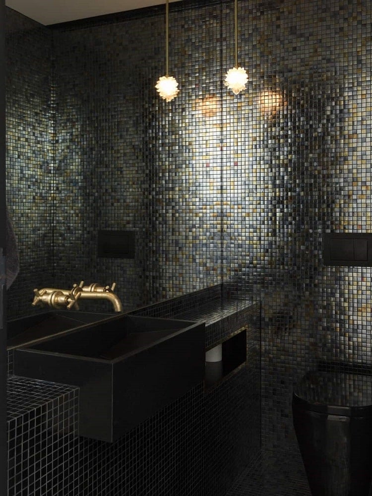 这是一个黑色的化妆室，展示了黑色墙壁瓷砖的独特外观，与黑色水槽和黑色厕所完美搭配，并辅以大镜子。