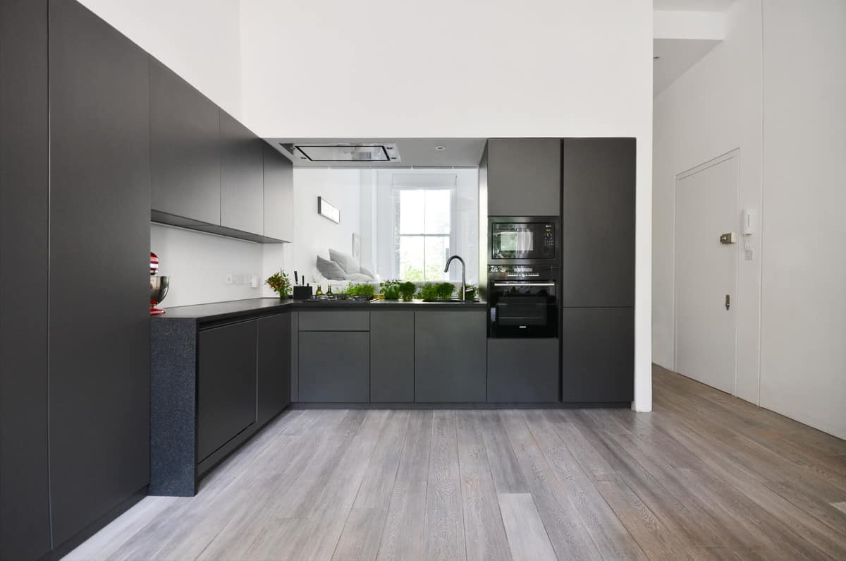 极简主义的黑色厨房，配有现代橱柜，黑色台面和黑色电器。然而，高耸的墙壁是白色的，与中等硬木地板一起给空间带来了一些亮度。