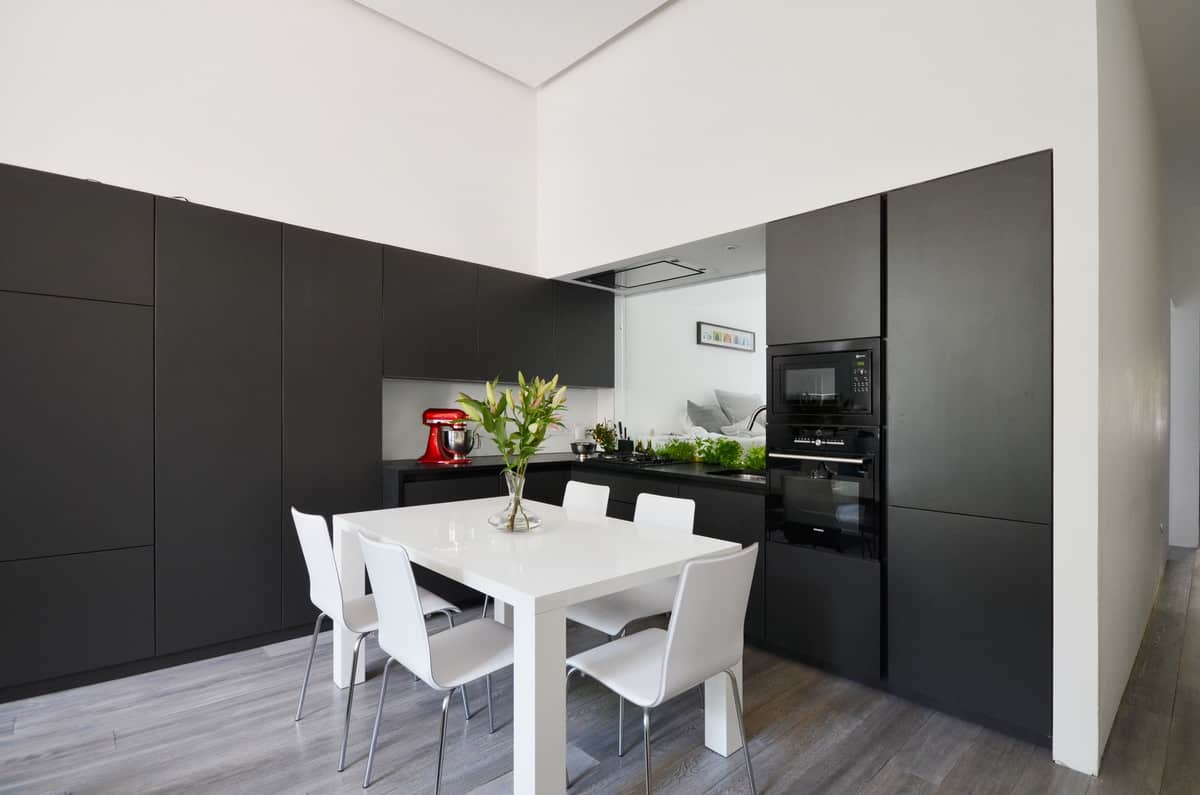 小的l型现代黑色厨房，黑色电器，中间是明亮的白色餐桌，白色椅子。