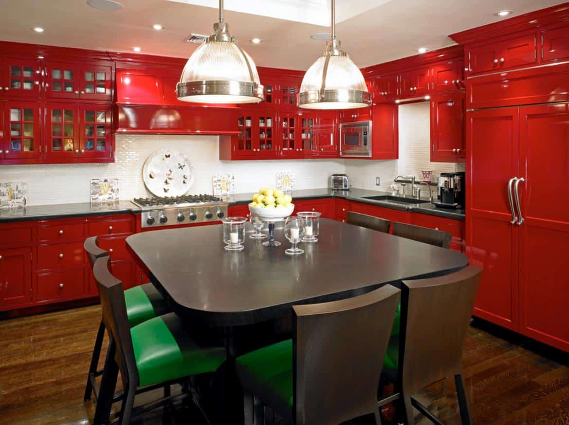 宽敞的红色橱柜厨房设计，上面有玻璃面橱柜和红色镶板冰箱。深色的木地板很好，但是厨房的桌子不太好，尤其是绿色的椅子。厨房餐桌用白色的东西会更好地与白色的地铁瓷砖和白色的天花板相呼应。