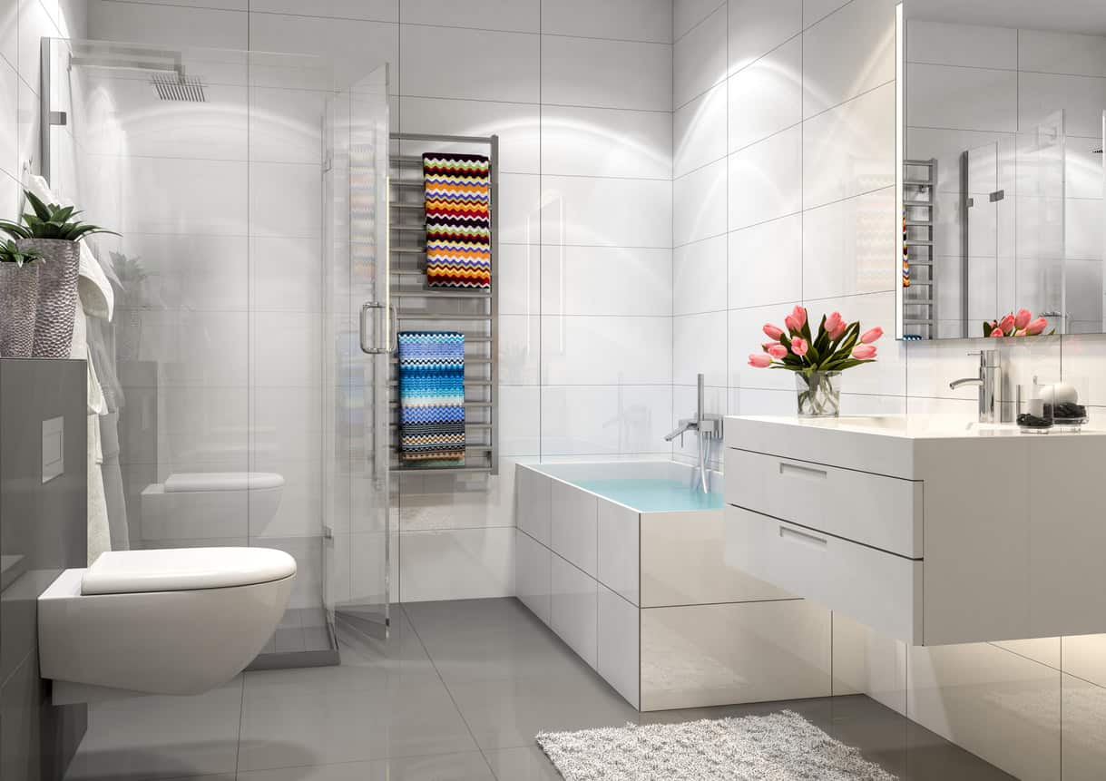 这是一间较小的现代主浴室，有浮动的白色梳妆台、小浴缸、浮动马桶和小玻璃淋浴间，地板是灰色的，墙壁是白色的。壁挂式金属加热毛巾架是一个很好的触感。
