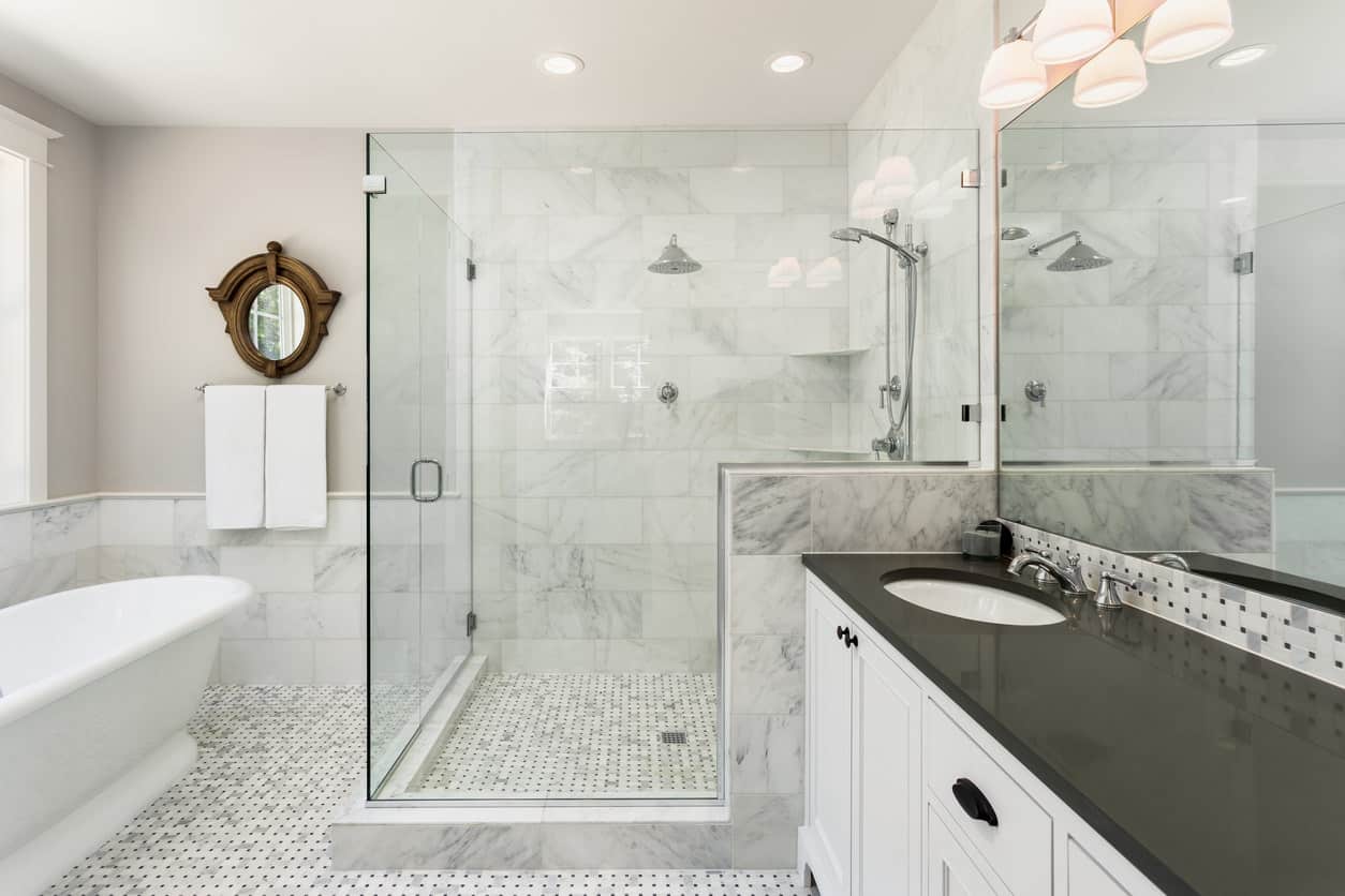 这种风格的主浴室在今天非常常见，有灰色和白色的瓷砖地板，独立的白色浴缸，黑色表面的白色梳妆台和全玻璃步入式淋浴(非常大)。