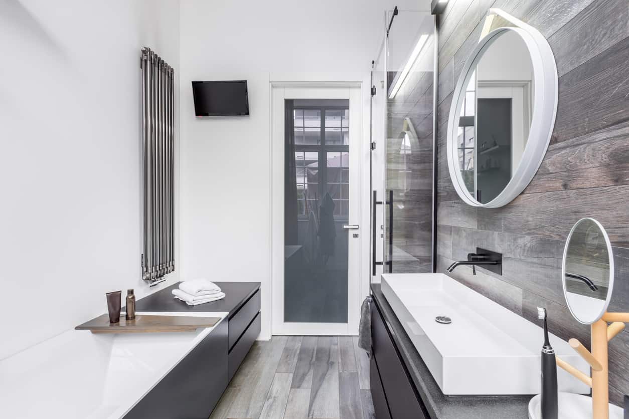 质朴与现代在这个主要的浴室，质朴的木墙，圆形镜子，然后是现代橱柜和超现代的槽式盆。
