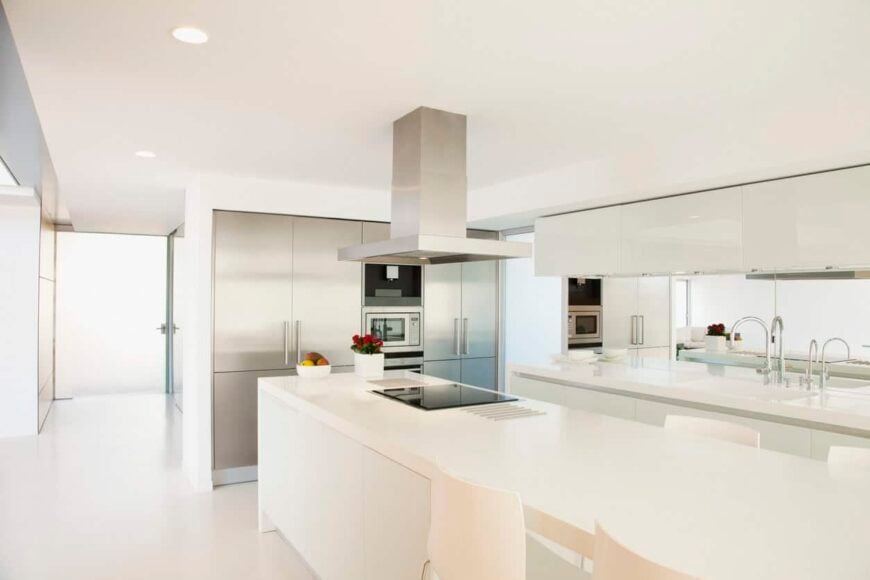 这是一个鲜明的白色当代厨房设计，具有超长岛和极简主义的氛围。