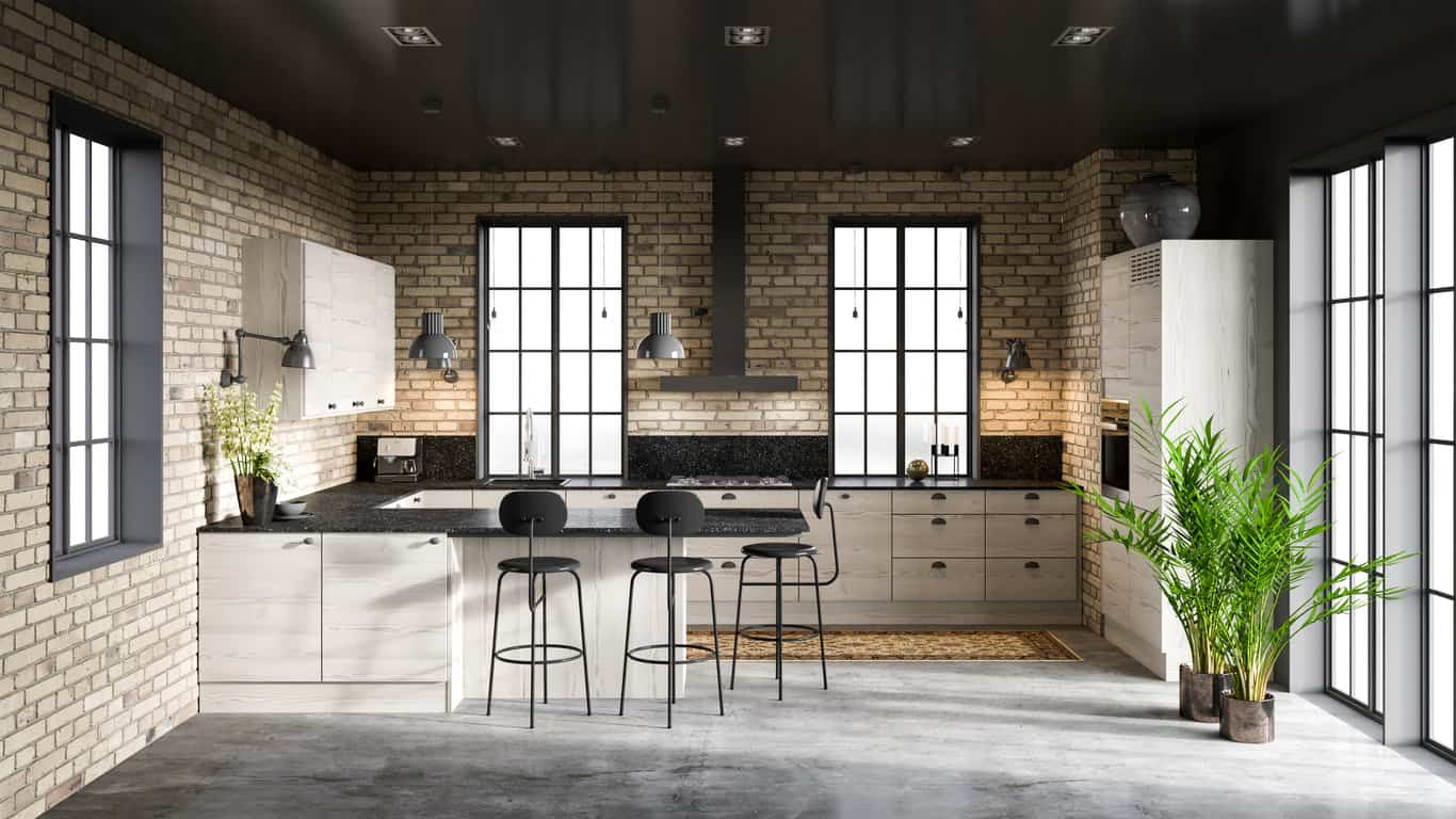 工业阁楼厨房，黑色台面，黑色橱柜硬件，黑色油烟机和黑色天花板。这是一个融合了黑色的厨房的例子，由于轻质砖墙、白色橱柜和窗户，看起来不会太暗。