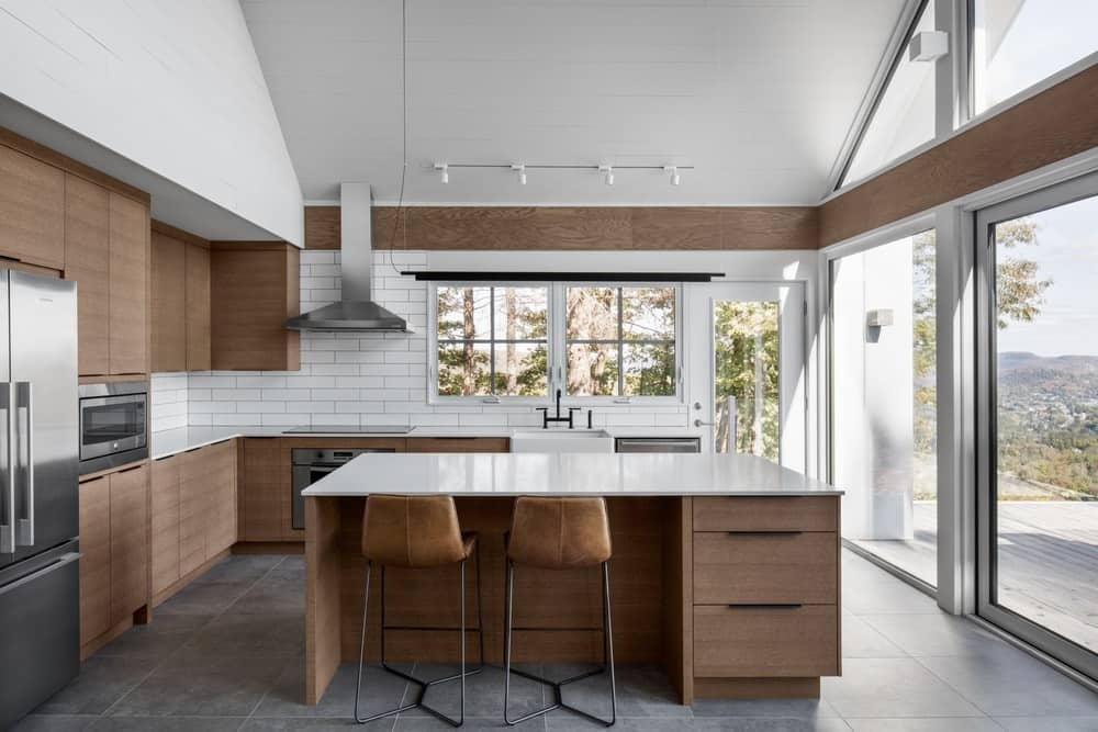 l型厨房配有棕色橱柜、厨房柜台和一个中央岛台，以及白色瓷砖后挡板和白色台面。