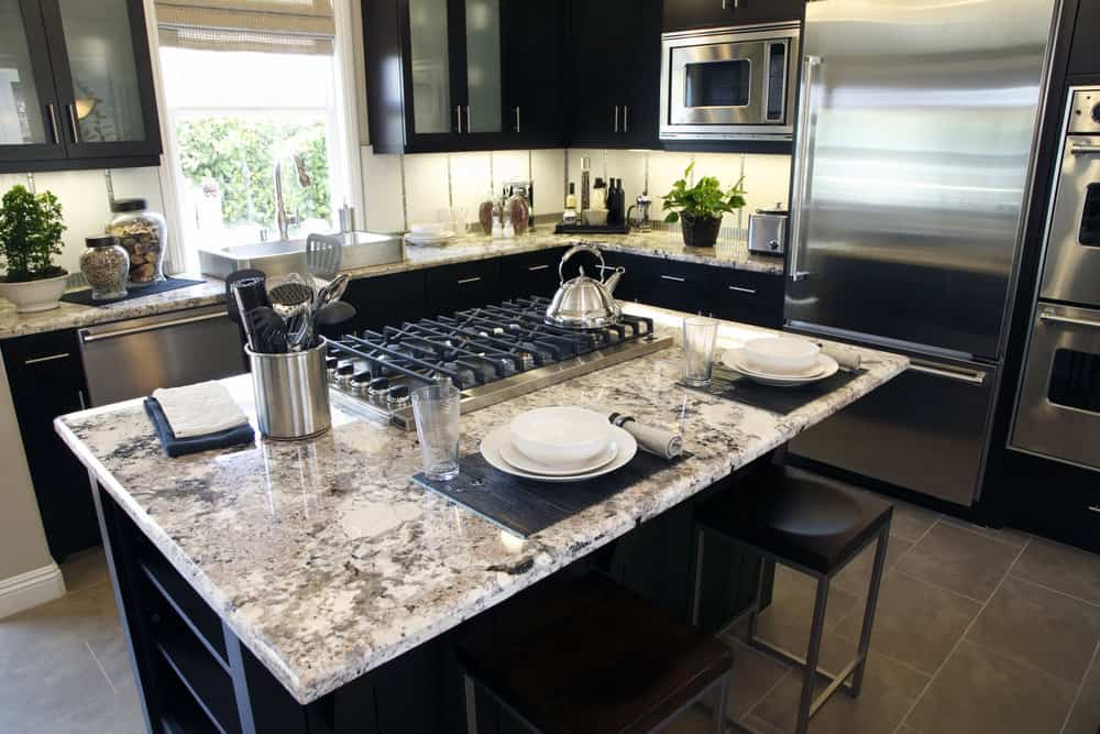 传统的厨房风格，各种黑色厨柜，不锈钢电器，大型白色矩形水槽和米色/深棕色花岗岩表面。