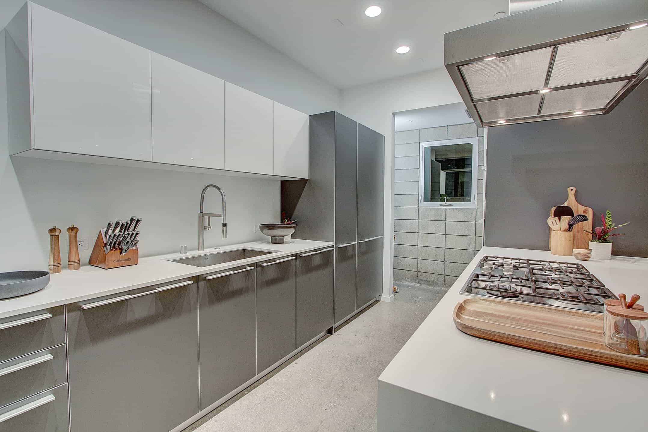 厨房以灰色的厨房柜台和中央岛台为特色，都有光滑的白色台面，并由嵌入式天花板灯照明。