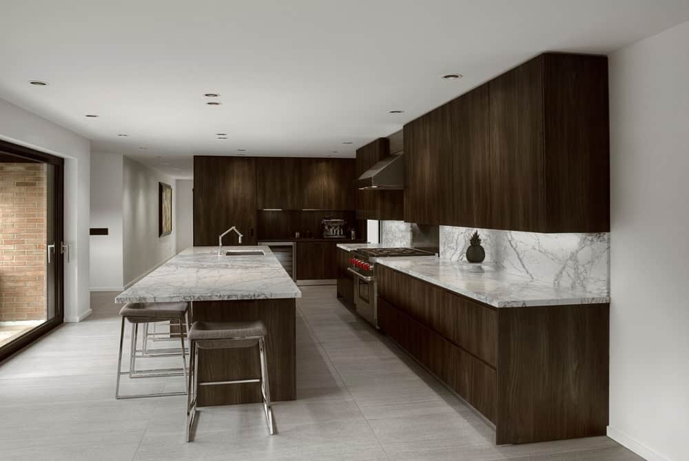 厨房里有棕色的橱柜，厨房柜台和一个棕色的中央岛台，带厚大理石台面和后挡板。