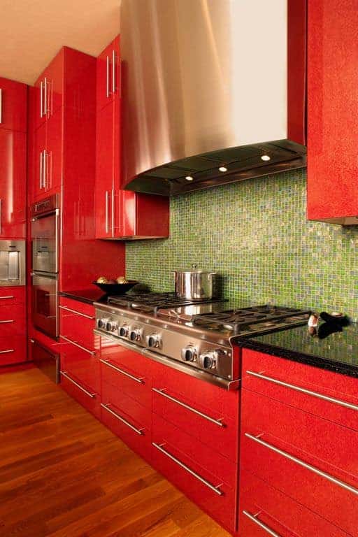 明亮的红色厨房橱柜与铬五金的特写。后挡板是绿色的瓷砖，木地板是红色的。我不太喜欢绿色的后挡板，但我很喜欢那种特别的红色。