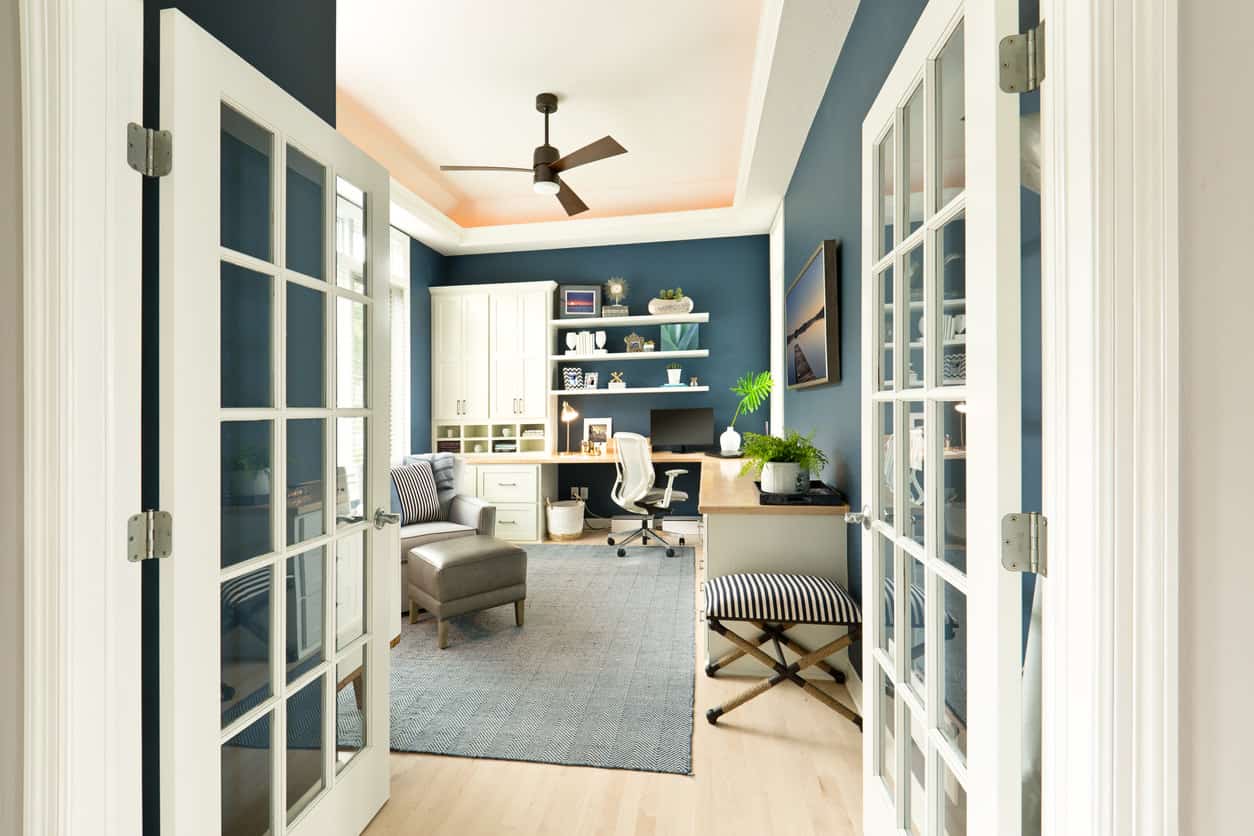 这个家庭办公室以l形的办公桌为特色，周围环绕着时尚的蓝色墙壁。托盘天花板看起来非常漂亮。