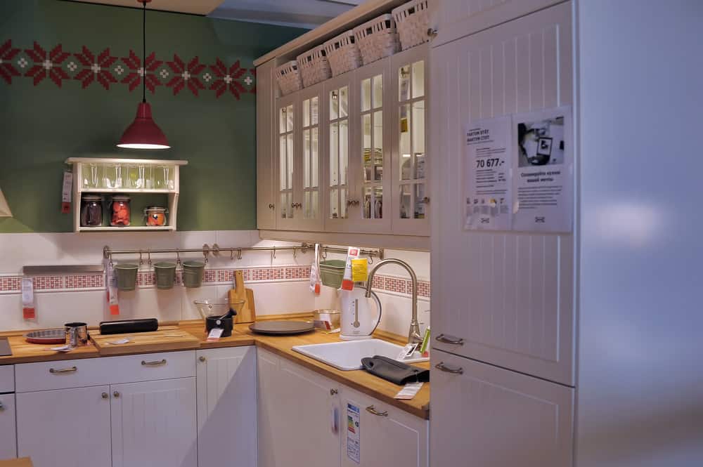 这个小厨房里的家具和固定装置都是鲜奶油的颜色。厨房的前墙下铺着瓷砖，但上半部分被漆成森林绿色。柜子顶部的柳条篮子给人一种走进林中小屋厨房的错觉。